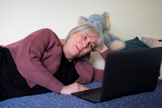 Mature woman smiling softly while watching laptop during video call at home
