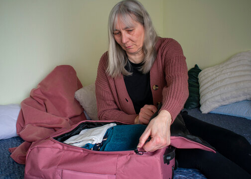 Close up of senior woman closing suitcase zipper while packing