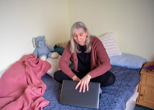 Senior woman working on laptop sitting cross legged on bed at home