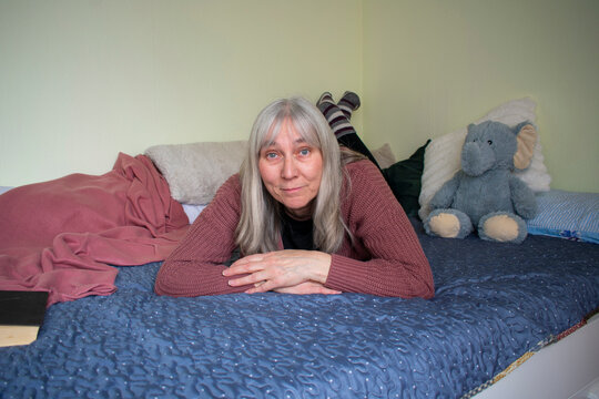 Senior woman lying on bed looking at camera with calm and friendly expression