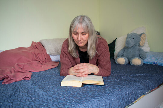 Senior woman reading a book while lying on bed in a calm home environment