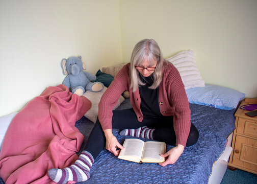 Senior woman sitting on bed reading a book in a quiet moment at home