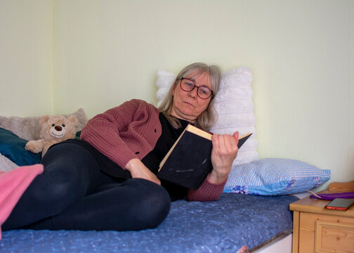 Senior woman lying on bed reading a book in a quiet and peaceful moment at home