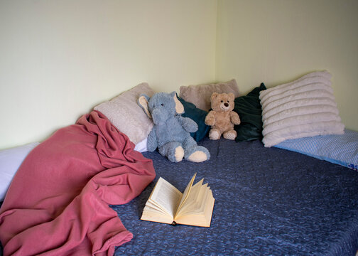 Open book on bed with pillows and stuffed toys in cozy bedroom interior