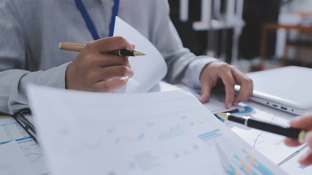 Two accountants examining financial documents using a calculator, taking notes, and discussing results, surrounded by documents and technology in a busy office environment. Audit and taxes in business