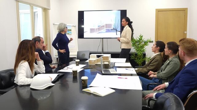 Two diverse female architects delivering a presentation on a new architectural project to a group of colleagues in a modern office boardroom