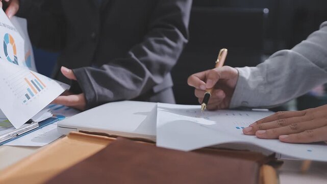 Two accountants examining financial documents using a calculator, taking notes, and discussing results, surrounded by documents and technology in a busy office environment. Audit and taxes in business