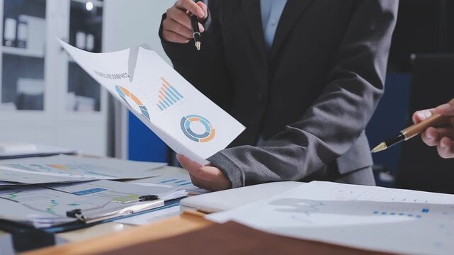 Two accountants examining financial documents using a calculator, taking notes, and discussing results, surrounded by documents and technology in a busy office environment. Audit and taxes in business