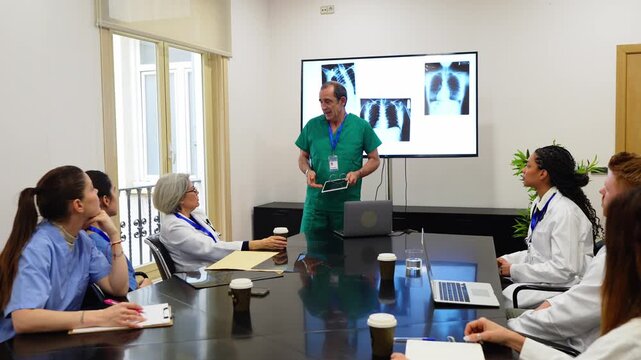 Surgeon leading a clinical meeting, presenting a lung diagnosis using chest x rays to a team of doctors and nurses in a hospital boardroom