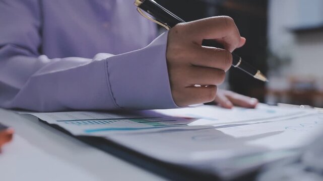 Two accountants examining financial documents using a calculator, taking notes, and discussing results, surrounded by documents and technology in a busy office environment. Audit and taxes in business