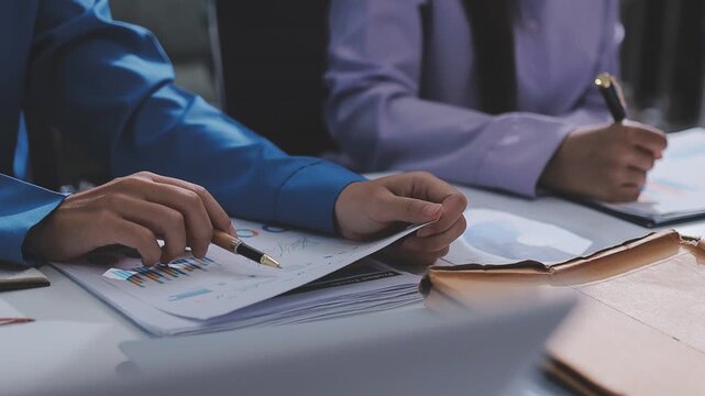 Two accountants examining financial documents using a calculator, taking notes, and discussing results, surrounded by documents and technology in a busy office environment. Audit and taxes in business