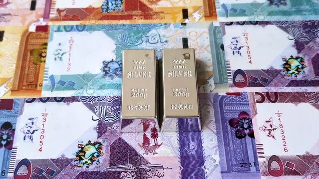 A silver bar, white metal against a backdrop of Qatari money, as a concept for the sales market. A silver bar as a background for your design