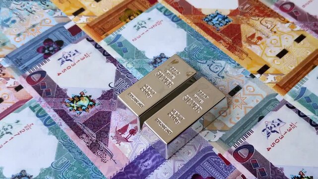 A silver bar, white metal against a backdrop of Qatari money, as a concept for the sales market. A silver bar as a background for your design