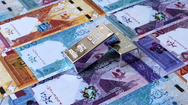 A silver bar, white metal against a backdrop of Qatari money, as a concept for the sales market. A silver bar as a background for your design