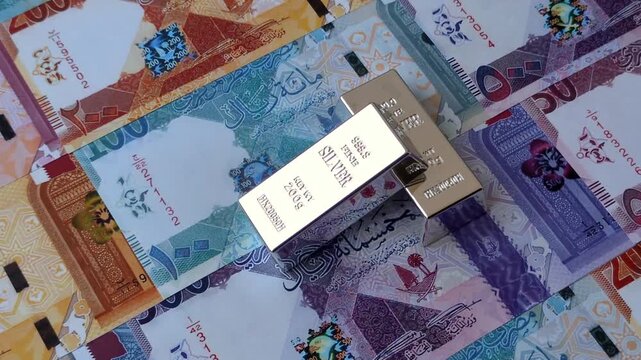 A silver bar, white metal against a backdrop of Qatari money, as a concept for the sales market. A silver bar as a background for your design