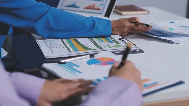 Two accountants examining financial documents using a calculator, taking notes, and discussing results, surrounded by documents and technology in a busy office environment. Audit and taxes in business