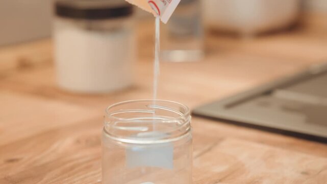 Warm light illuminates kitchen during powder refilling. Aesthetic scene of powder being carefully added to jar. Serene kitchen moment with powder pouring into jar under cozy ambient lighting