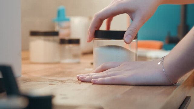 Sweet jar stay. Calm baker reaches for lid amidst cozy kitchen. Home baker gently picks up jar of sugar on counter. Peaceful moment as baker reaches for sugar jar in warm kitchen setting