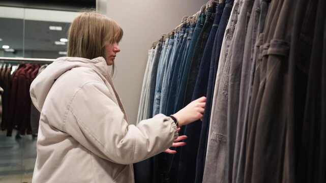 Young teenage customer selecting jeans in clothing shop, showcasing consumer behavior, fashion retail experience, and everyday shopping decisions in modern store.
