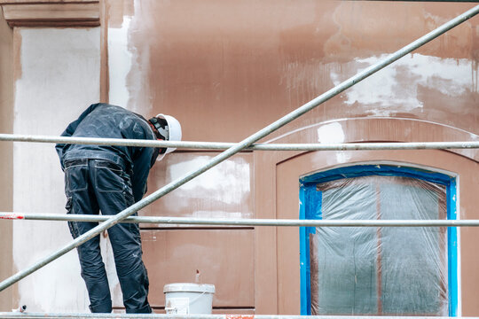 Unrecognizable construction worker standing on scaffolding and renovating building facade