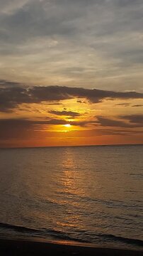 Beautiful golden sunset over a black sand beach with calm sea water and colorful evening sky. Peaceful coastal scenery with warm sunlight reflection, located at Singaraja, Bali, Indonesia.