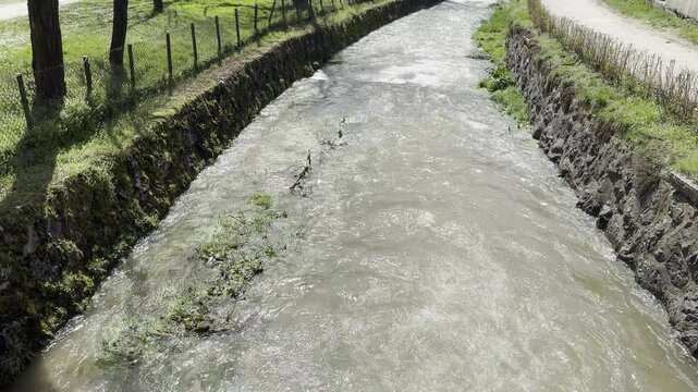 Fast flowing muddy river water in a stone canal during spring