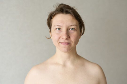 Woman Facing Camera Neutral Expression Standing Against Plain Indoor Background With Bare Shoulders Natural Light Soft Skin Closeup Portrait For Personal Care Concept.