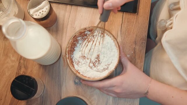 Overhead hands dusting pastry with powdered sugar, milk bottle and jars on wooden board, styling props for breakfast shoot, warm morning light, home cooking scene with food blogger styling