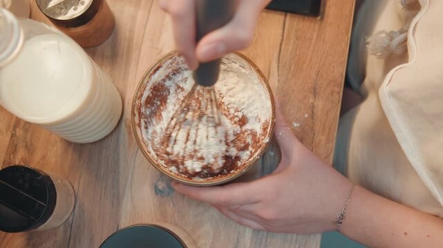Overhead view of tart dusting, hands holding tart on wooden board, milk bottle and ramekin beside, cocoa and powdered sugar creating decorative pattern, warm natural light, intimate home cooking