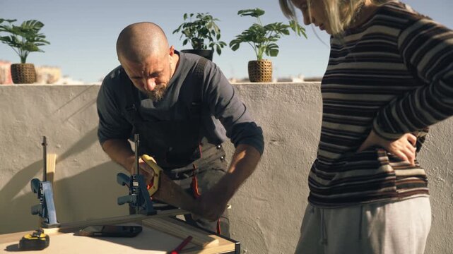 Father in work uniform teaching teenage daughter how to saw wooden board for school DIY project outdoors, guiding her through practical learning process.