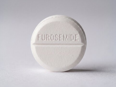 A professional photography close-up shot of a scored white round pill with FUROSEMIDE stamped into the top half, presented on a uniform neutral background.