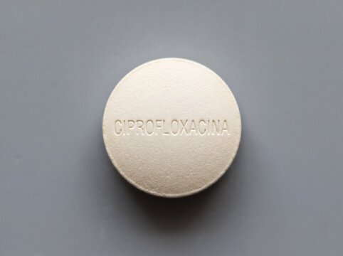 A professional photography close-up shot of a round film-coated tablet with CIPROFLOXACINA engraved on the surface, set against a smooth neutral background.