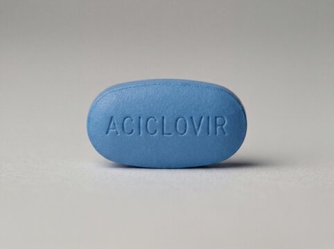 A professional photography close-up shot of a blue oval tablet with ACICLOVIR clearly stamped on the front, resting on a plain neutral background.