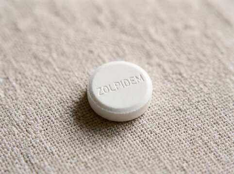 A professional photography close-up shot of a small circular tablet with ZOLPIDEM engraved on the surface, set against a smooth neutral background.