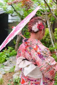 Woman wearing a traditional kimono holds a pink parasol in a garden in Kyoto Japan