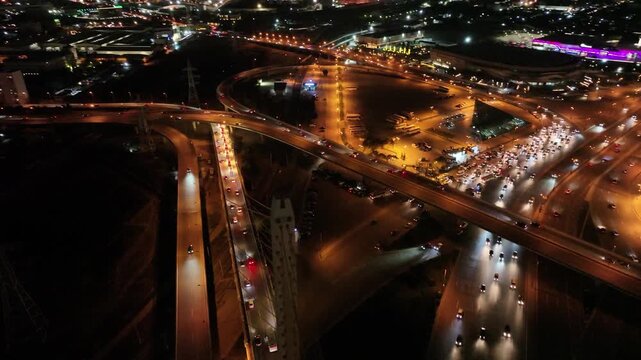 Aerial Nightscape of Urban Interchanges: A breathtaking aerial view showcases a complex network of glowing highways and traffic, illuminated by the vibrant lights of a bustling city at night.