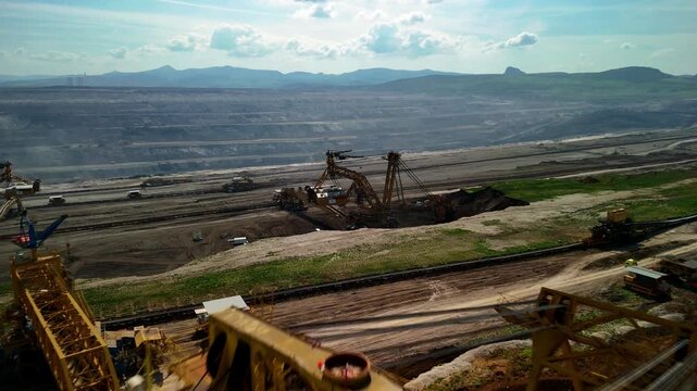 Horizontal drone footage flying close above the upper structure of a bucket wheel excavator before revealing additional mining machines and the vast quarry landscape on the horizon.
