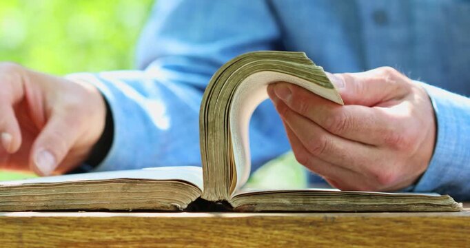 Flipping pages in old vintage book by male hands against nature green background. Education, reading leisure outdoor and holy bible concept.