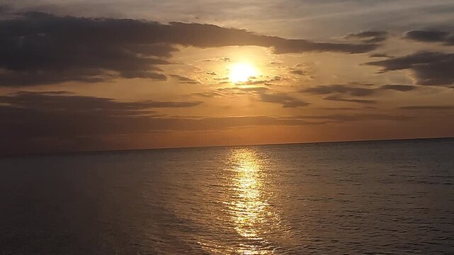 Beautiful golden sunset over a black sand beach with calm sea water and colorful evening sky. Peaceful coastal scenery with warm sunlight reflection, located at Singaraja, Bali, Indonesia.
