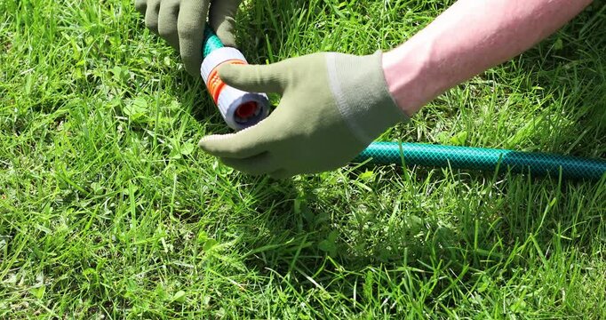 Gardener hands coupling two garden hoses with fastening fitting on green lawn. Watering system for irrigation preparation, diy gardening maintenance.