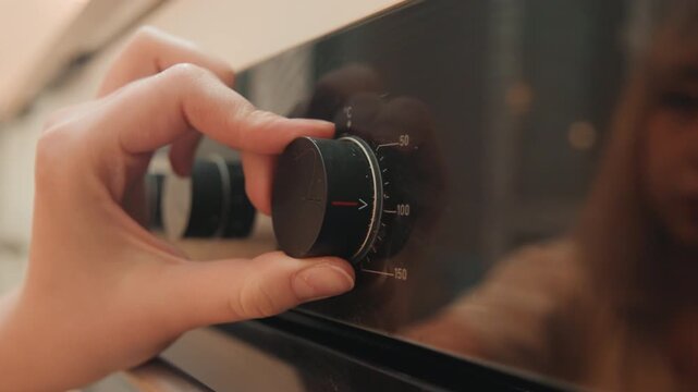 Focused hand adjusts oven knob in kitchen. Individual turns oven dial with intent in modern culinary space. Precise action of hand setting oven dial reflecting calm domestic cooking preparation