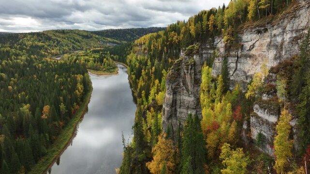 Autumn river winding through a forested gorge beneath sheer limestone cliffs, viewed from a high vantage with golden foliage, rugged rock faces, and a calm waterway under clouds