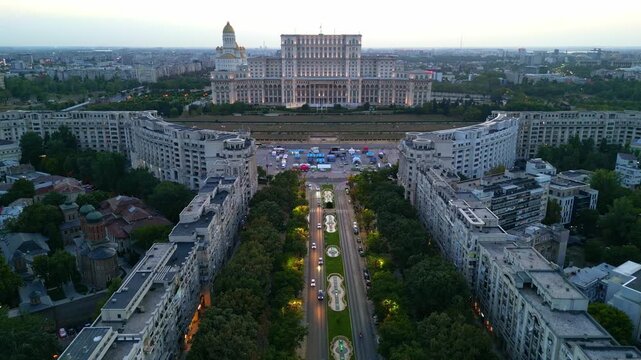 High angle twilight view of the Palace of the Parliament in Bucharest, Romania. Famous heavy building landmark with glowing city lights at sunset.
