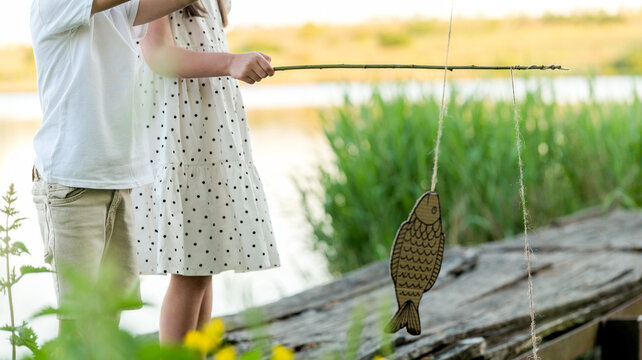 Children pretend fishing with a handmade fish on a stick by the water