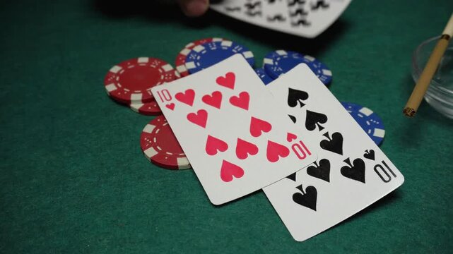 Hand placing playing cards on a stack of poker chips during a card game on a green felt table with visible poker accessories in the background