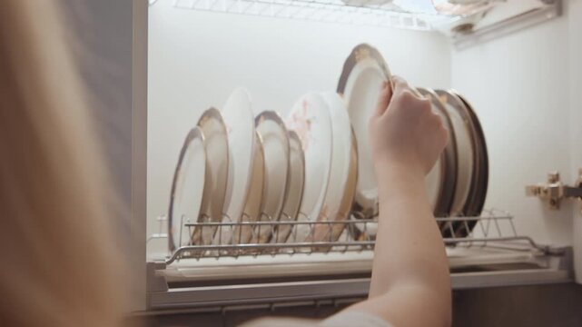 Kitchen dish organization. Placing porcelain dishes carefully. Gentle hands arrange fine ceramicware. Tidy kitchen scene with carefully stored porcelain plates after cooking session