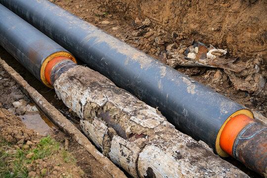 Old district heating pipes with outdated insulation being replaced by new insulated pipes in excavation trench, utility renovation and infrastructure modernization