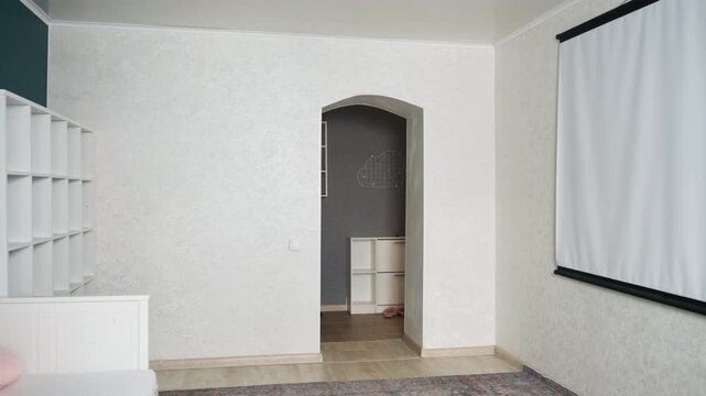 Empty living room ready for cleaning, neutral textured wall and projector screen, builtin shelving and doorway visible, decluttered modern interior, soft natural light, peaceful staged atmosphere