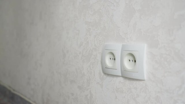 Electrical cord removal process. Carefully disconnecting wire from socket with attention. Closeup shot capturing safe unhooking of electrical cord adjacent to textured wallpaper and baseboard