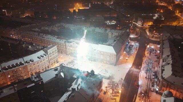 Bright Fireworks over a City Square with Buildings and Winter Streets during New Year Night